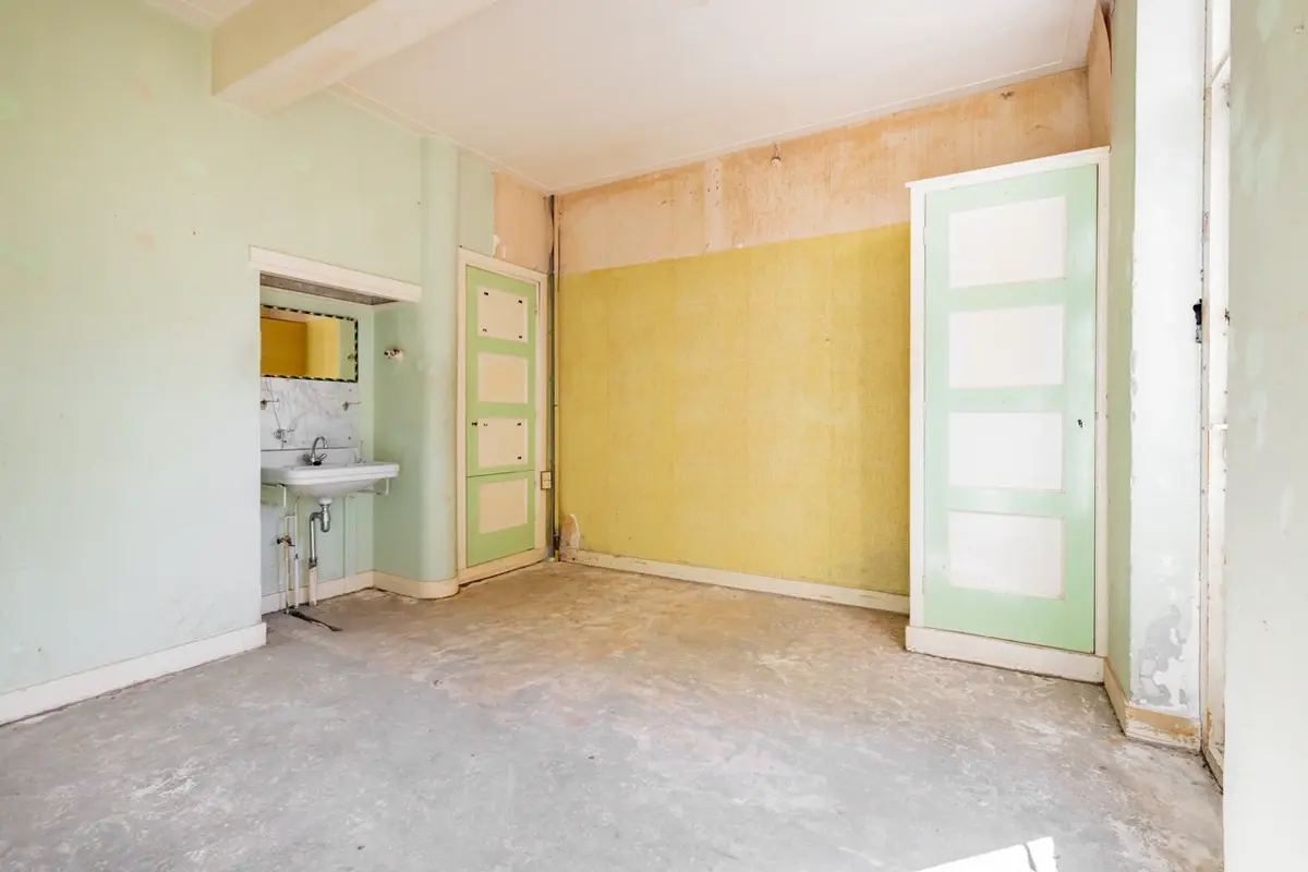 Slaapkamer van een kluswoning met oud behang en een fonteintje