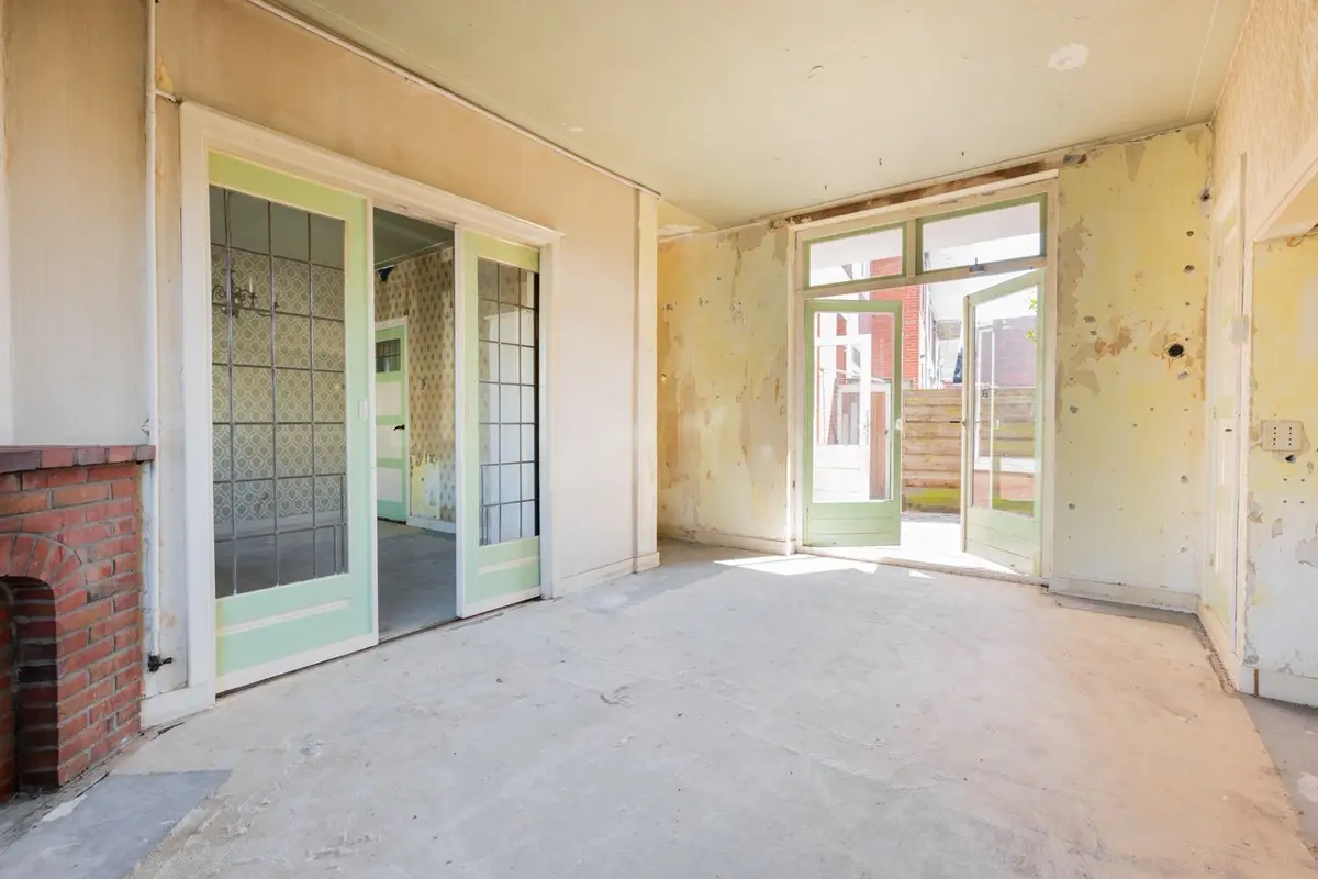 Woonkamer van een kluswoning met kale wanden en betonvloer